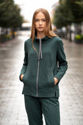Comfortable dark green women's two-piece tracksuit made of soft brushed-inside cotton jersey; features a full-zip hoodie with decorative stitched pockets, high collar, subtle side slits and straight-cut trousers with an elastic waistband. The set is designed for everyday wear, offering warmth, softness and a clean silhouette. / Tamsiai žalios spalvos moteriškas trikotažinis laisvalaikio kostiumėlis su švelniu pūkeliu viduje, dekoratyvinėmis kišenėmis, aukšta apykakle, užtrauktuku ir tiesaus kirpimo kelnėmis