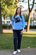 Blue womens leisure suit with 3/4 sleeve sweatshirt and black pants, soft cotton fabric with elastane, handmade front detail, side slits, pockets in sweatshirt and pants, elastic waistband trousers, comfortable everyday outfit, Lithuanian design Jakas, mėlynas moteriškas laisvalaikio kostiumas su rankų darbo detale, patogios kelnės su guma ir kišenėmis, kasdieniam dėvėjimui