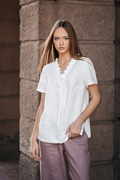 Balta lininė palaidinė moterims – trumpomis rankovėmis, dekoruota subtiliomis klostelėmis aplink kakliuką ir per priekį, siūta iš minkštinto natūralaus lino – White linen blouse for women with delicate pleated detail and short sleeves, perfect for summer wear.