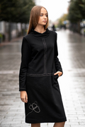 Juoda trikotažinė suknelė tiesaus silueto, su dekoratyvinėmis siūlėmis ir rankų darbo aplikacija, modelis stovi miesto gatvėje – black knit dress with decorative seams, handmade applique, straight silhouett