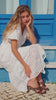 Moteris vilki ilgą baltą medvilninę suknelę su angliškais siuvinėjimais. Suknelė turi pasijonį, trumpas rankoves, gilią V formos iškirptę ir platėjančią apačią. Elegantiškas, romantiškas ir lengvas vasaros derinys, pasiūtas iš 100 % natūralios medvilnės.