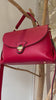 Raudona natūralios odos rankinė iš Prancūzijos su dviem skyriais, užsegamais užtrauktukais, dekoratyviniu atvartu su metaline saga, trumpa rankenėle ir ilgu 115 cm dirželiu, geltono metalo furnitūra, išmatavimai 33x19x14 cm.
