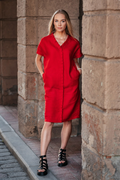 A woman wearing a bright red linen dress with a V neckline and decorative pleats in the front. The dress features short dropped sleeves and side pockets. Ryškiai raudona lininė suknelė su klostėmis ir kišenėmis.